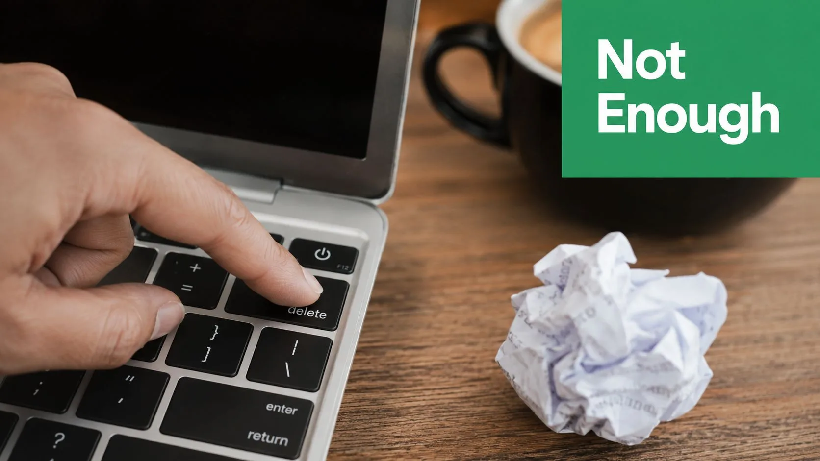 A hand pressing the delete key on a laptop keyboard next to a crumpled paper ball.